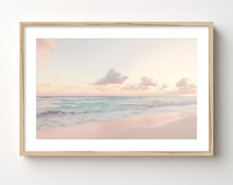 Può includere: Una stampa incorniciata di una scena di spiaggia. L'immagine presenta una spiaggia di sabbia rosa, acqua turchese e un cielo pastello con nuvole rosa. La cornice in legno aggiunge un tocco naturale al sereno paesaggio costiero.