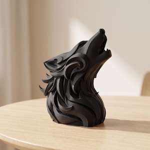 Könnte beinhalten: Eine mattschwarze Skulptur eines Wolfskopfes in heulender Pose. Das Objekt weist stilisierte, geschichtete Fellstrukturen auf, die ein Gefühl von Bewegung und Tiefe erzeugen. Der Wolf ist mit nach oben gerichtetem Fang dargestellt.