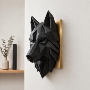 May include: A matte black wolf head wall sculpture featuring a geometric, faceted design. The wolf head is mounted on a rectangular, metallic gold base plate, creating a sharp contrast between the dark, angular form and the bright, flat backing.