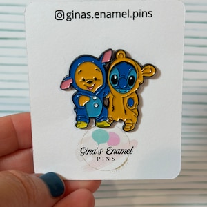May include: Enamel pin featuring Winnie the Pooh and Stitch wearing matching blue and yellow pajamas. The pin is on a white card with the text "ginas.enamel.pins" and "Gina's Enamel Pins".