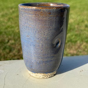 May include: A blue and brown ceramic mug with a textured glaze. The mug has a slightly uneven rim and a white base.