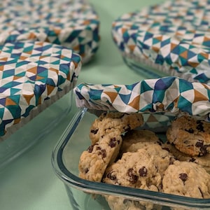 Peut inclure: Gros plan sur un récipient en verre rempli de cookies aux pépites de chocolat, recouvert d'un couvercle en tissu réutilisable. Le couvercle présente un motif géométrique en bleu sarcelle, marron et blanc.