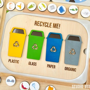 Könnte beinhalten: Ein hölzerner Spielzeug-Recycling-Behälter mit vier Fächern, die mit "Plastik", "Glas", "Papier" und "Organisch" beschriftet sind. Jedes Fach hat einen Ausschnitt eines Recycling-Behälters mit einem Recycling-Symbol. Das Spielzeug ist dazu gedacht, Kindern das Recycling beizubringen.