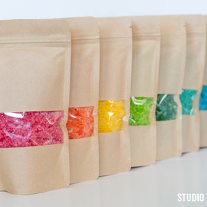 May include: Ten brown paper bags with clear windows, each filled with colorful bath salts. The colors of the salts are pink, orange, yellow, green, light green, blue, teal, and purple.