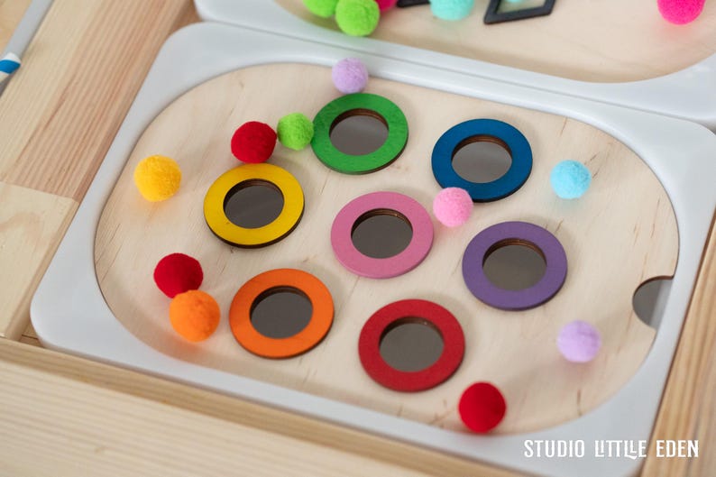 May include: A wooden toy with colorful rings and pom-poms. The rings are different colors, including red, orange, yellow, green, blue, purple, and pink. The pom-poms are also different colors, including red, orange, yellow, green, blue, purple, and pink. The toy is designed for children to play with and learn about colors.