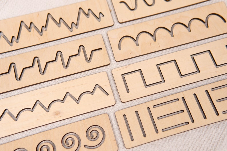 May include: A collection of wooden tracing boards with various cut-out line patterns. The boards are rectangular and made of light-colored wood. The patterns include zigzags, waves, and geometric shapes, designed for tracing and fine motor skill development.