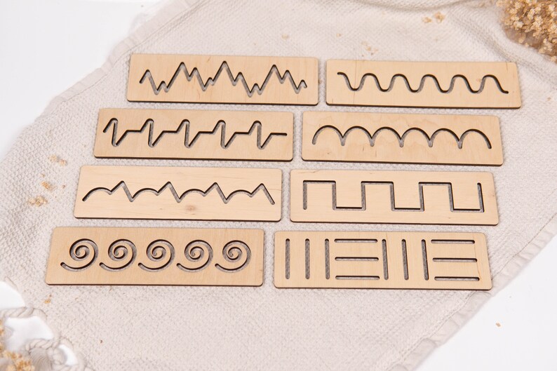 May include: A set of eight wooden tracing boards with various line patterns. The boards are rectangular and feature cut-out designs of wavy lines, zigzags, spirals, and other shapes. The natural wood color provides a neutral background for the patterns.