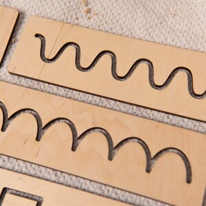May include: Wooden tracing boards with various cut-out shapes, including zigzags, waves, and curves. The boards are made of light-colored wood and are designed for educational purposes. The shapes are approximately 4 inches long.