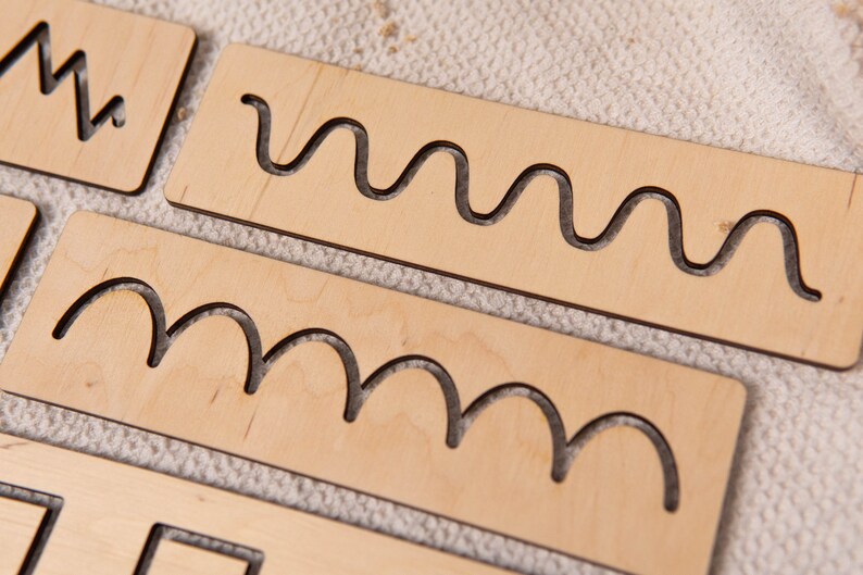 May include: Wooden tracing boards with various cut-out shapes, including zigzags, waves, and curves. The boards are made of light-colored wood and are designed for educational purposes. The shapes are approximately 4 inches long.