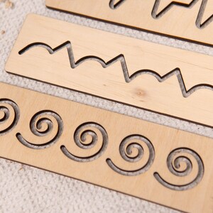 May include: Wooden tracing boards with various cut-out patterns, including zigzags and spirals. The boards are made of light-colored wood and are designed for early childhood education and fine motor skill development.