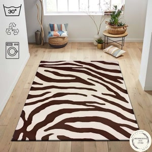 Op de afbeelding: Een bruin en wit zebraprint tapijt met een witte achtergrond en bruine strepen. Het tapijt is machinewasbaar op 30 graden Celsius. Het tapijt heeft een label met de tekst "Made with love, Mesmerizing Rug Store, For You".