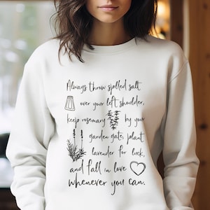 May include: White sweatshirt with a black graphic print that reads "Always throw spilled salt over your left shoulder, keep rosemary by your garden gates, plant lavender for luck, and fall in love whenever you can."