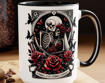 May include: White ceramic mug with a black rim and handle. The mug features a black and white illustration of two skeletons holding a bouquet of red roses. The skeletons are surrounded by red roses and butterflies. The text "Eternal Love, Eternal Darkness" is printed on a banner at the bottom of the mug.