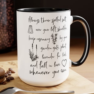 May include: White ceramic mug with a black handle and rim. The mug has a black and white design with text that reads "Always throw spilled salt over your left shoulder, keep rosemary by your garden gate, plant lavender for luck, and fall in love whenever you can."