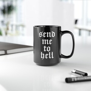 Puede incluir: Taza de café de cerámica negra con texto blanco que dice "send me to hell" en una fuente gótica.