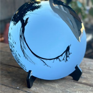 K&ouml;nnte beinhalten: Ein runder, blauer, reflektierender Spiegel mit einem schwarzen St&auml;nder. Der Spiegel reflektiert einen Baum und den Himmel.