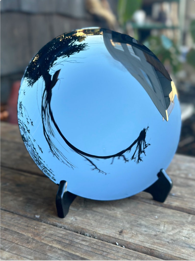 K&ouml;nnte beinhalten: Ein runder, blauer, reflektierender Spiegel mit einem schwarzen St&auml;nder. Der Spiegel reflektiert einen Baum und den Himmel.