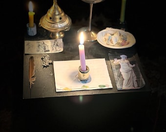 May include: A dimly lit scene featuring a black table with various items. A lit purple candle is in the center, surrounded by other candles, a chalice, a decorative incense burner, and small illustrations. A feather and a seashell dish are also present.