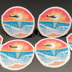 May include: Six round stickers with a sunset over the ocean and a silhouette of a helicopter flying in the sky. The stickers are printed on white paper with a glossy finish.