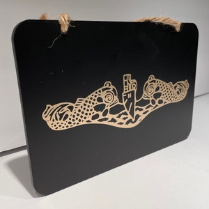 May include: A black wooden sign with a gold-colored submarine emblem. The emblem features a submarine with two dolphins flanking it.