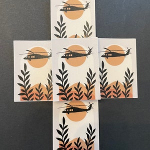 May include: Five black and white stickers with a silhouette of a helicopter flying over a stylized sunset with orange and brown hills and black leaves.