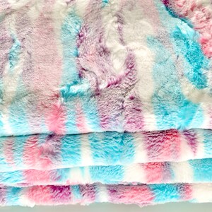 May include: A soft, plush fabric with a tie-dye pattern in shades of pink, blue, and purple. The fabric is folded in layers, showing the different colors.