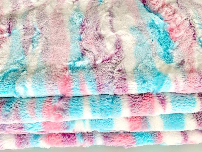 May include: A soft, plush fabric with a tie-dye pattern in shades of pink, blue, and purple. The fabric is folded in layers, showing the different colors.