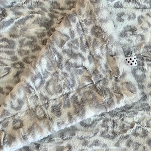 May include: A soft, white and gray faux fur throw blanket with a leopard print pattern.