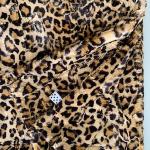 May include: A brown and black leopard print faux fur throw blanket. The blanket is folded in half and has a white tag with black polka dots.
