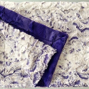 May include: A soft, plush blanket with a white and purple swirl pattern. One side is a solid purple color.