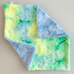 Puede incluir: Una manta suave y mullida para bebé con un patrón tie-dye en tonos azules, verdes y amarillos.