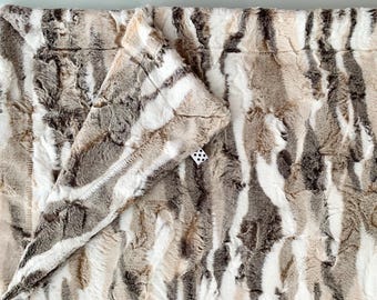 May include: A soft, plush throw blanket with a striped pattern in shades of brown, white, and grey. The blanket is made of faux fur and has a luxurious feel.