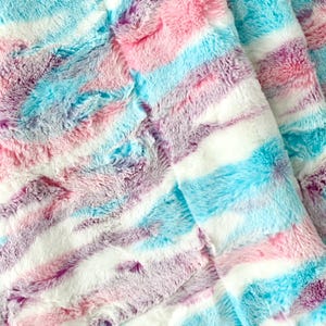 May include: A soft, fluffy blanket with a striped pattern in shades of pink, blue, and purple.