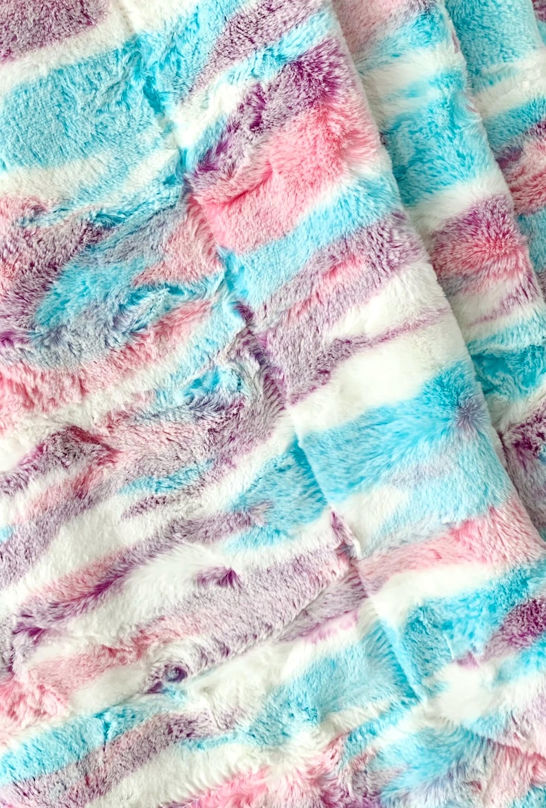 May include: A soft, fluffy blanket with a striped pattern in shades of pink, blue, and purple.