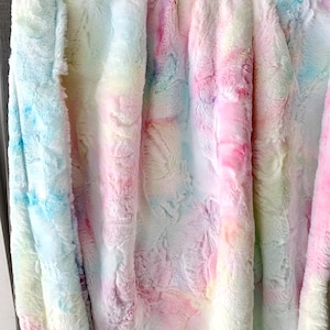 Könnte beinhalten: Eine weiche, flauschige Decke mit einem Batik-Muster in Rosa-, Blau- und Gelbtönen.