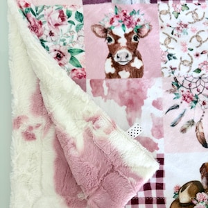 May include: A patchwork blanket featuring a soft pink and white plush backing. The front displays squares with a brown and white calf wearing a floral crown, pink roses, a dreamcatcher, maroon buffalo plaid, and the text She is fierce.