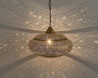 Op de afbeelding: Een messingkleurige hanglamp met een geperforeerd ontwerp, dat ingewikkelde patronen van licht en schaduw op het omringende oppervlak werpt. De lamp hangt aan een ketting en creëert een warme sfeer. De armatuur heeft een diameter van ongeveer 30 cm.
