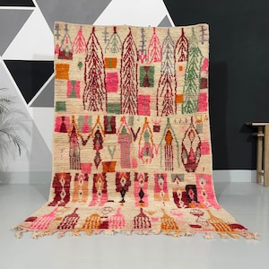 May include: Beige and multi-coloured area rug with geometric and abstract patterns. The rug features a cream-coloured background with designs in pink, orange, green, and burgundy. The rug has a fringed edge.