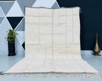 May include: Cream-colored, rectangular rug with a geometric design. The rug features a series of rectangular and linear patterns in a lighter cream color. The edges are finished with a black and white checkered border and fringe.