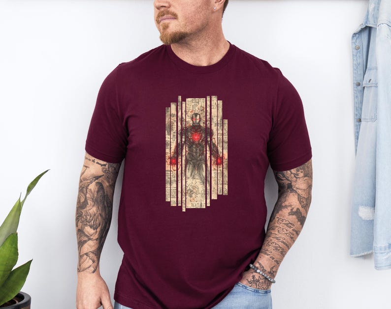 May include: Burgundy t-shirt featuring a detailed illustration of a superhero in a suit of armor. The graphic has a vintage, blueprint-like aesthetic with red accents. The design is centered on the chest of the shirt.