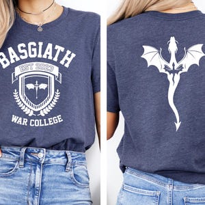 May include: A navy blue t-shirt with a white graphic design on the front. The design features a crest with the text "Basgiath Est 2023 War College". The back of the shirt features a white silhouette of a dragon.