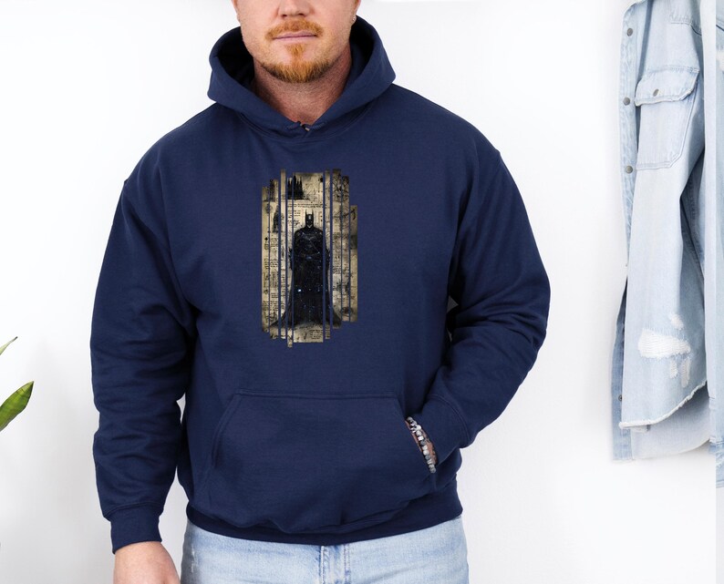 May include: Navy blue hooded sweatshirt featuring a Batman graphic. The graphic depicts Batman standing in a cage-like structure with a cityscape background. The sweatshirt has a front pocket and a drawstring hood.