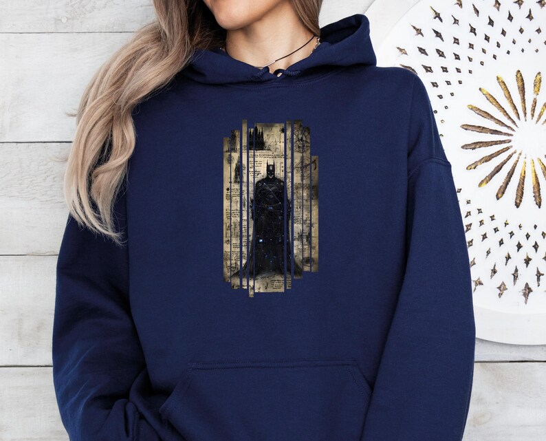 May include: Navy blue hoodie featuring a Batman graphic. The graphic depicts Batman standing behind bars, with a vintage-style background. The hoodie has a front pocket and a drawstring hood.