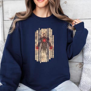 May include: Navy blue sweatshirt featuring a graphic of Iron Man. The design shows a detailed illustration of the character's armor and internal components, set against a backdrop of vertical, aged paper-like panels.