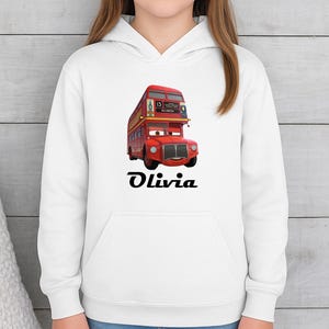 Puede incluir: Sudadera con capucha blanca con un dise&ntilde;o de autob&uacute;s de dos pisos de dibujos animados rojo y el nombre "Olivia" en negro. El autob&uacute;s tiene una cara sonriente. El dise&ntilde;o est&aacute; centrado.