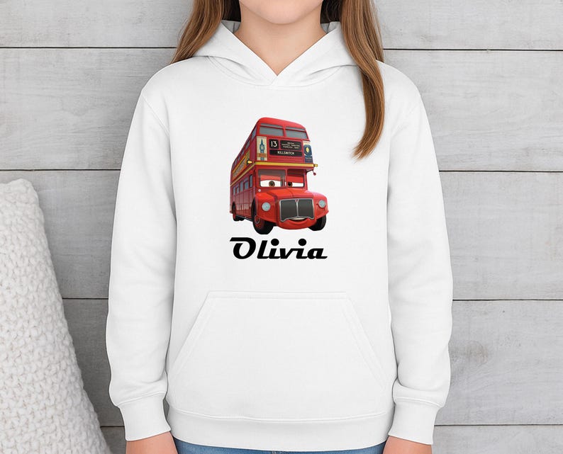 Puede incluir: Sudadera con capucha blanca con un dise&ntilde;o de autob&uacute;s de dos pisos de dibujos animados rojo y el nombre "Olivia" en negro. El autob&uacute;s tiene una cara sonriente. El dise&ntilde;o est&aacute; centrado.