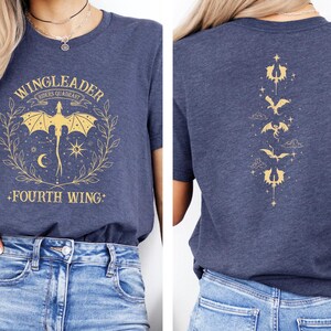 Pode incluir: Uma camiseta azul marinho com um gr&aacute;fico dourado de um drag&atilde;o e o texto "WINGLEADER", "RIDER'S QUADRANT" e "FOURTH WING". A parte de tr&aacute;s da camiseta tem um design vertical de cinco drag&otilde;es dourados.