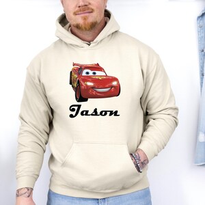 Puede incluir: Sudadera con capucha color crema con un gr&aacute;fico de coche de carreras rojo. El nombre "Jason" est&aacute; impreso en negro debajo. La sudadera tiene un bolsillo delantero y una capucha con cord&oacute;n.
