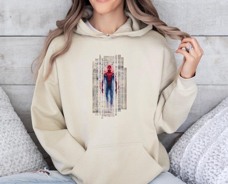 K&ouml;nnte beinhalten: Beiger Kapuzenpullover mit einer Grafik von Spider-Man in Rot und Blau. Der Superheld ist in einem vertikalen rechteckigen Design mit einem strukturierten, Vintage-Hintergrund dargestellt. Der Hoodie hat eine Vordertasche und eine Kapuze mit Kordelzug.