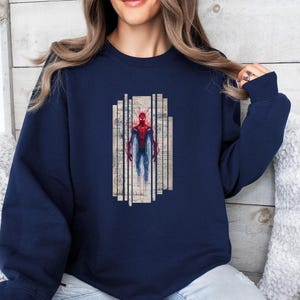 Op de afbeelding: Marineblauwe sweatshirt met een Spiderman-afbeelding. De afbeelding toont Spiderman in een rood-blauw pak, tegen een achtergrond van verticale lijnen en muzieknoten. De sweatshirt heeft lange mouwen en een ronde hals.